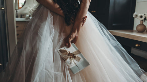 Back of bride with hands behind her back, holding letters that are tied with ribbon