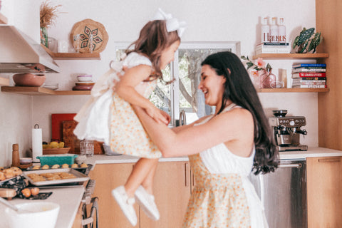 Woman laughing and carrying young girl to sit her on kitchen counter