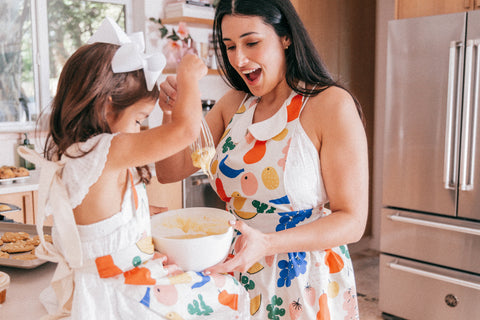 A woman and child baking together on the kitchen counter while wearing colorful retro aprons