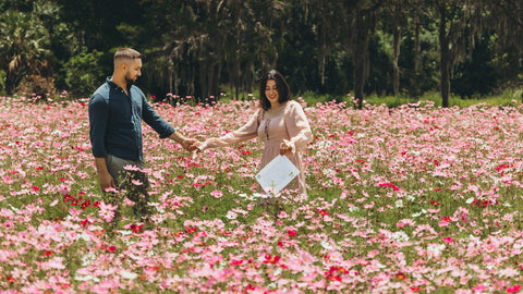 Man holding woman's hand in a vast pink flower field under the sun