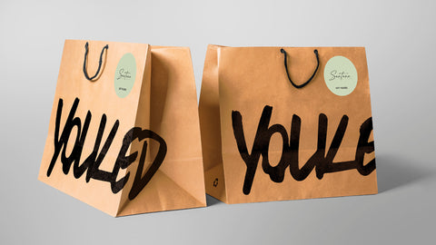Two brown carry out bags with a soft green sticker and black handles
